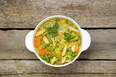 Photo of Saucepan of delicious vegetable soup with chicken on wooden table, top view