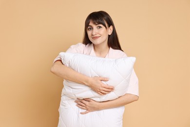 Photo of Woman wearing pyjama and holding pillow on beige background