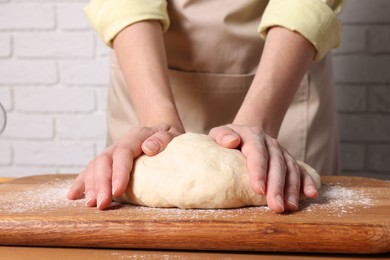 Woman kneading dough at wooden table near white brick wall, closeup