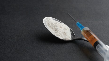 Spoon with powder, syringe on black background, closeup and space for text. Hard drugs