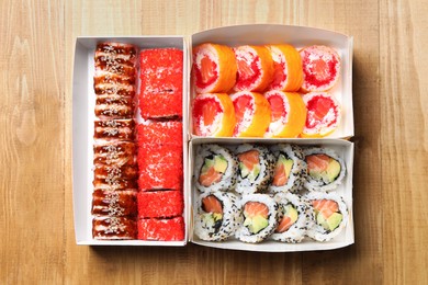 Photo of Food delivery. Paper boxes with delicious sushi rolls on wooden table, flat lay