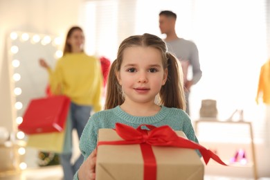 Photo of Little girl with gift box near her parents in store. Family Christmas shopping