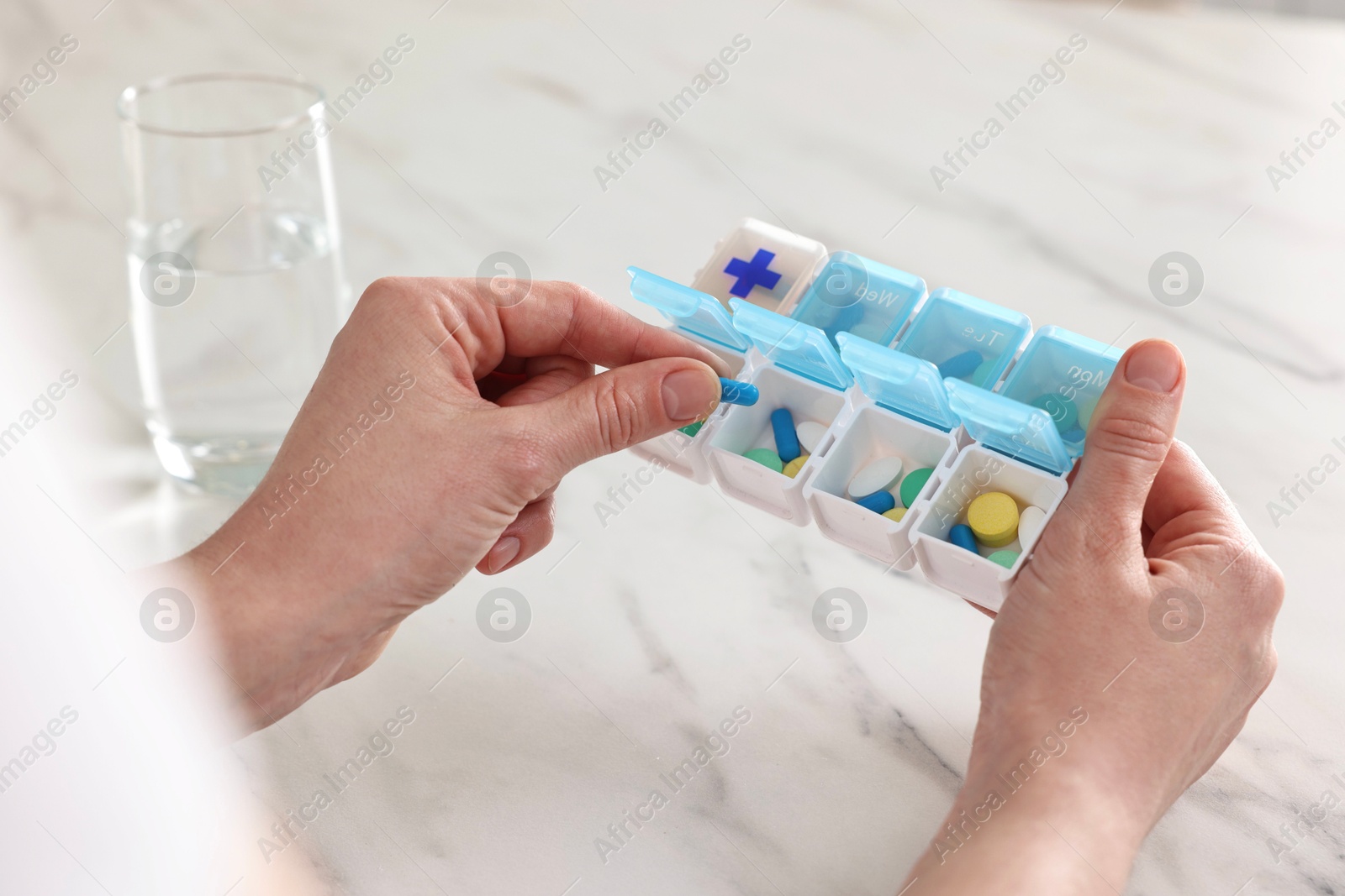 Photo of Woman with pills, organizer and glass of water at white marble table, closeup