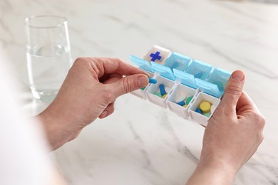 Photo of Woman with pills, organizer and glass of water at white marble table, closeup