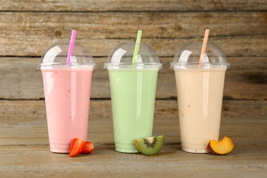 Photo of Plastic cups with different tasty smoothies and fresh fruits on wooden table