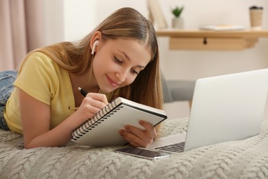 Teenage girl writing in notebook on bed at home