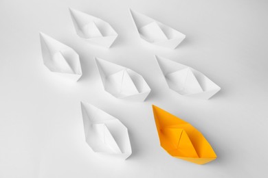 Photo of Group of paper boats following orange one on white background. Leadership concept