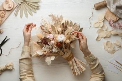 Photo of Florist making beautiful bouquet of dried flowers at white table, top view