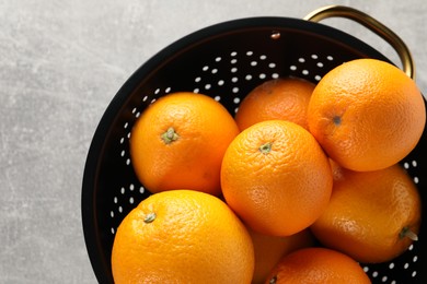 Photo of Fresh ripe oranges in black colander on light grey table, top view