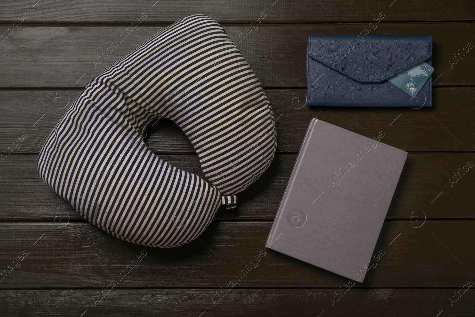 Photo of Striped travel pillow, notebook and wallet with credit card on dark wooden background, flat lay