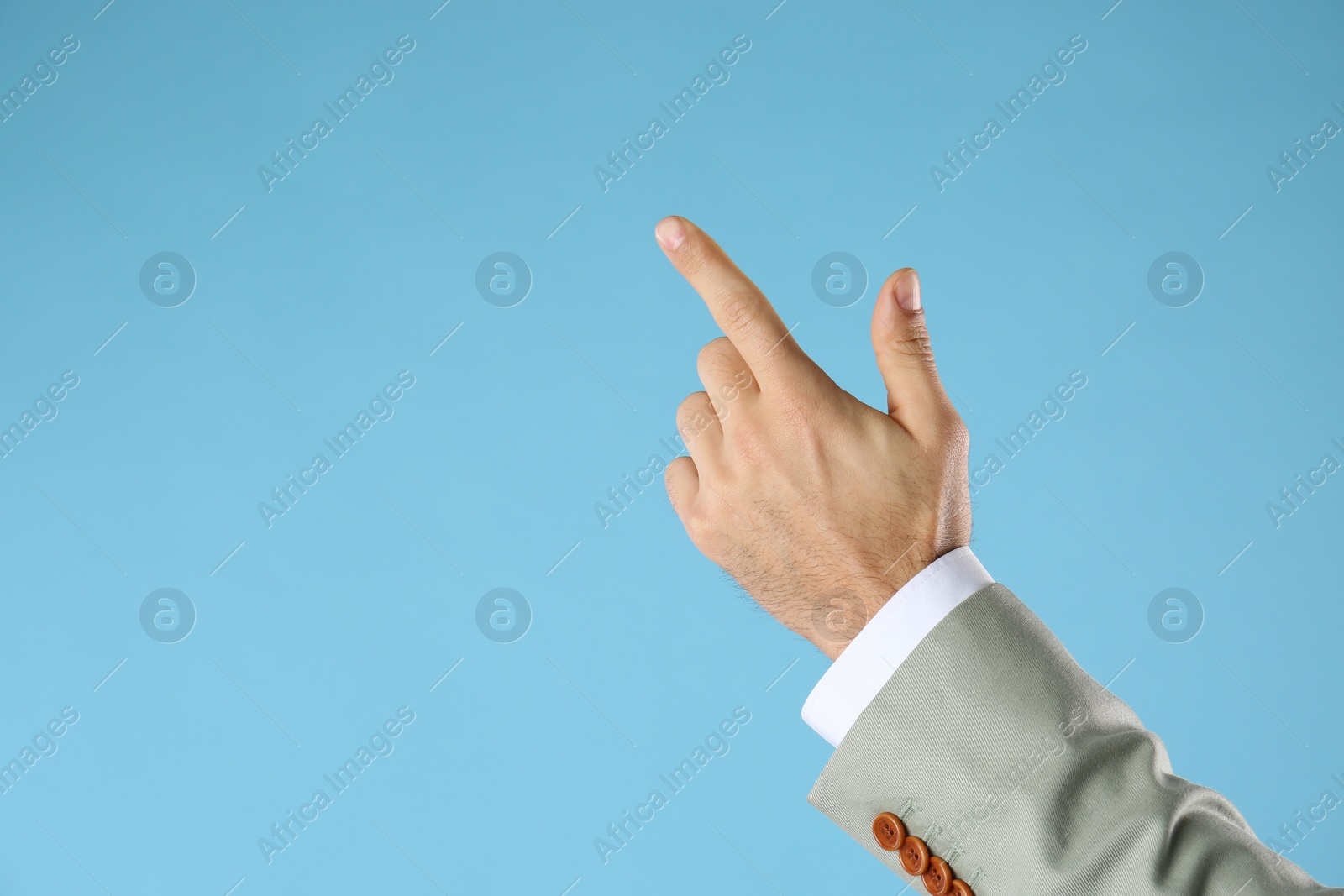 Photo of Businessman pointing at something on light blue background, closeup. Finger gesture