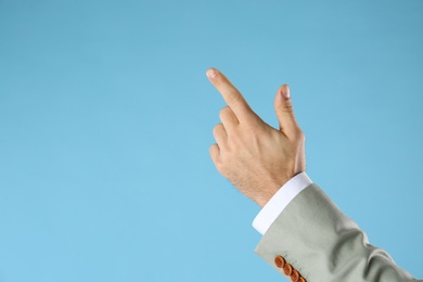 Businessman pointing at something on light blue background, closeup. Finger gesture