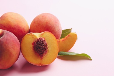 Whole and cut fresh ripe peaches on pink background, closeup