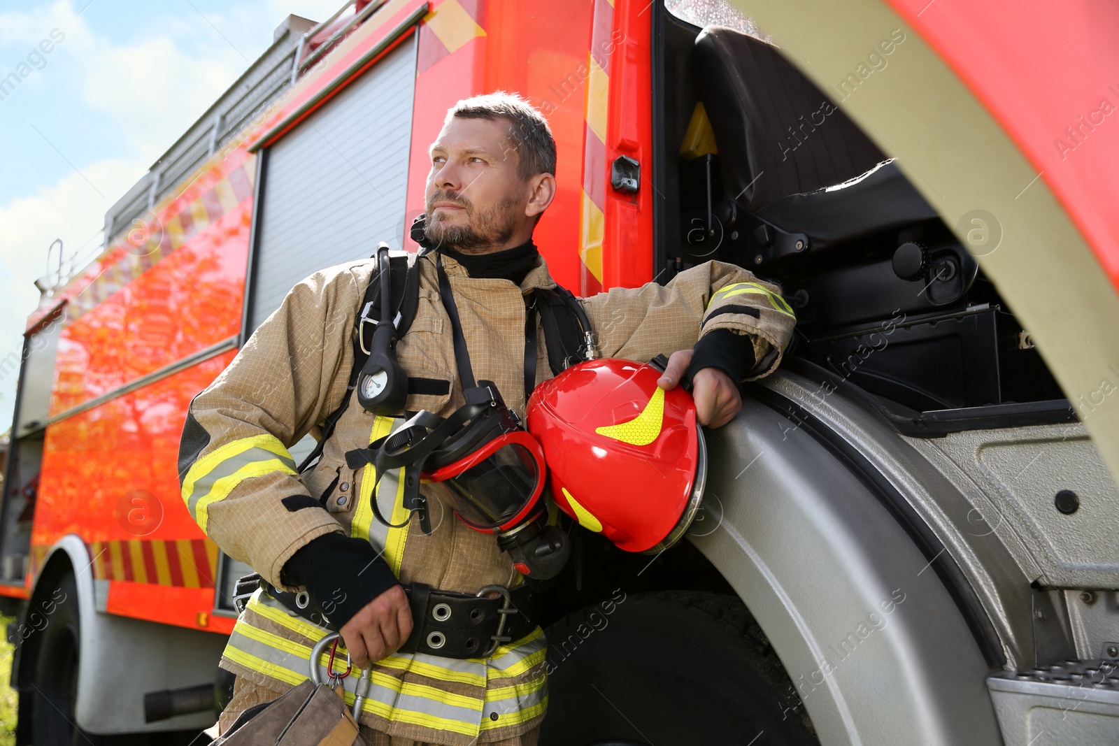 Photo of Firefighter in uniform with helmet near fire truck outdoors