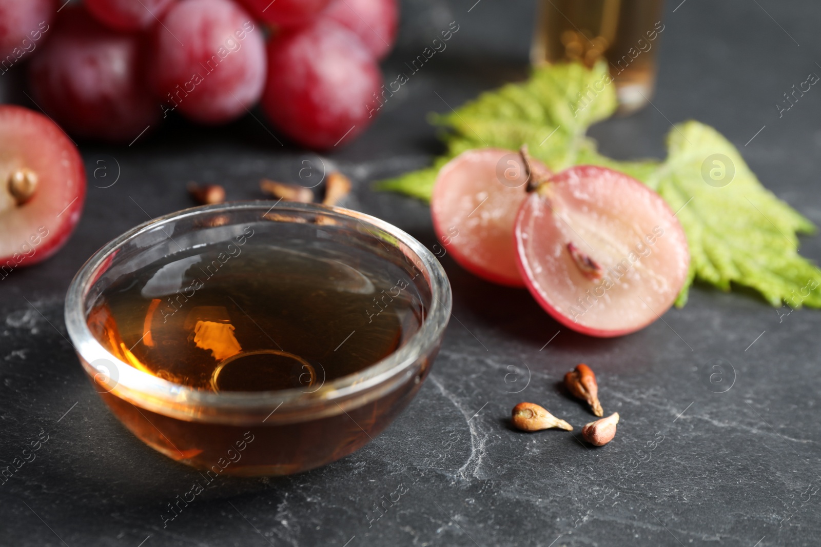 Photo of Bowl of natural grape seed oil on dark table. Organic cosmetic