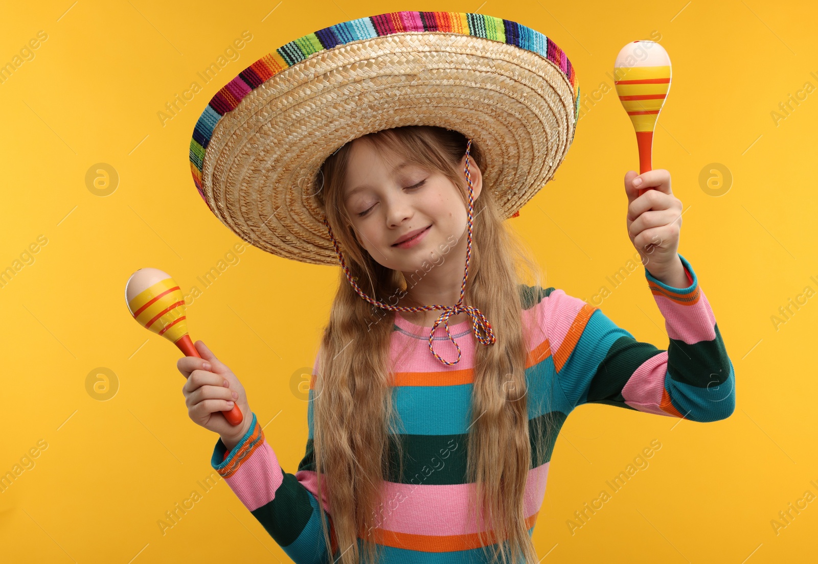 Photo of Cute girl in Mexican sombrero hat dancing with maracas on orange background