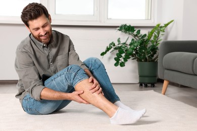 Photo of Man massaging leg on white carpet at home