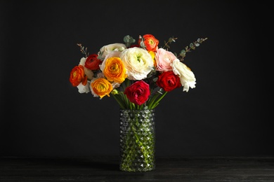 Vase with beautiful spring ranunculus flowers on table against dark background