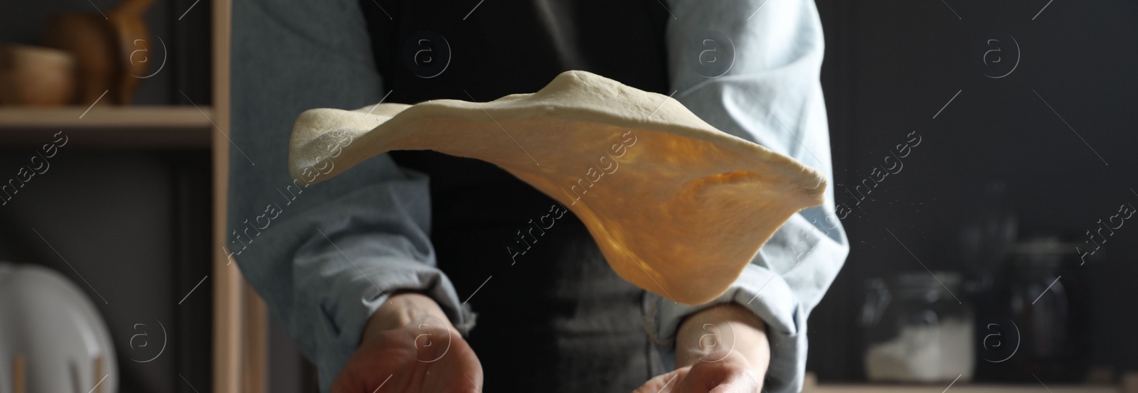 Photo of Woman tossing pizza dough in kitchen, closeup