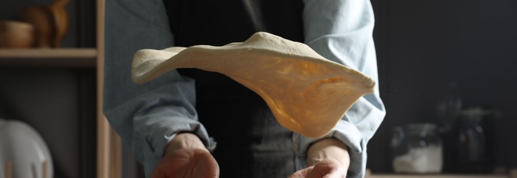 Photo of Woman tossing pizza dough in kitchen, closeup