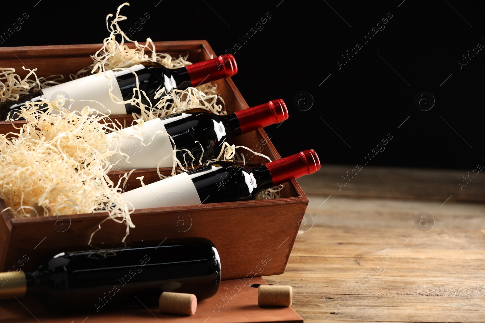 Photo of Box with wine bottles on wooden table against black background. Space for text