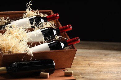 Photo of Box with wine bottles on wooden table against black background. Space for text