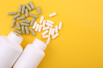 Jars with different vitamin capsules on yellow background, flat lay. Space for text