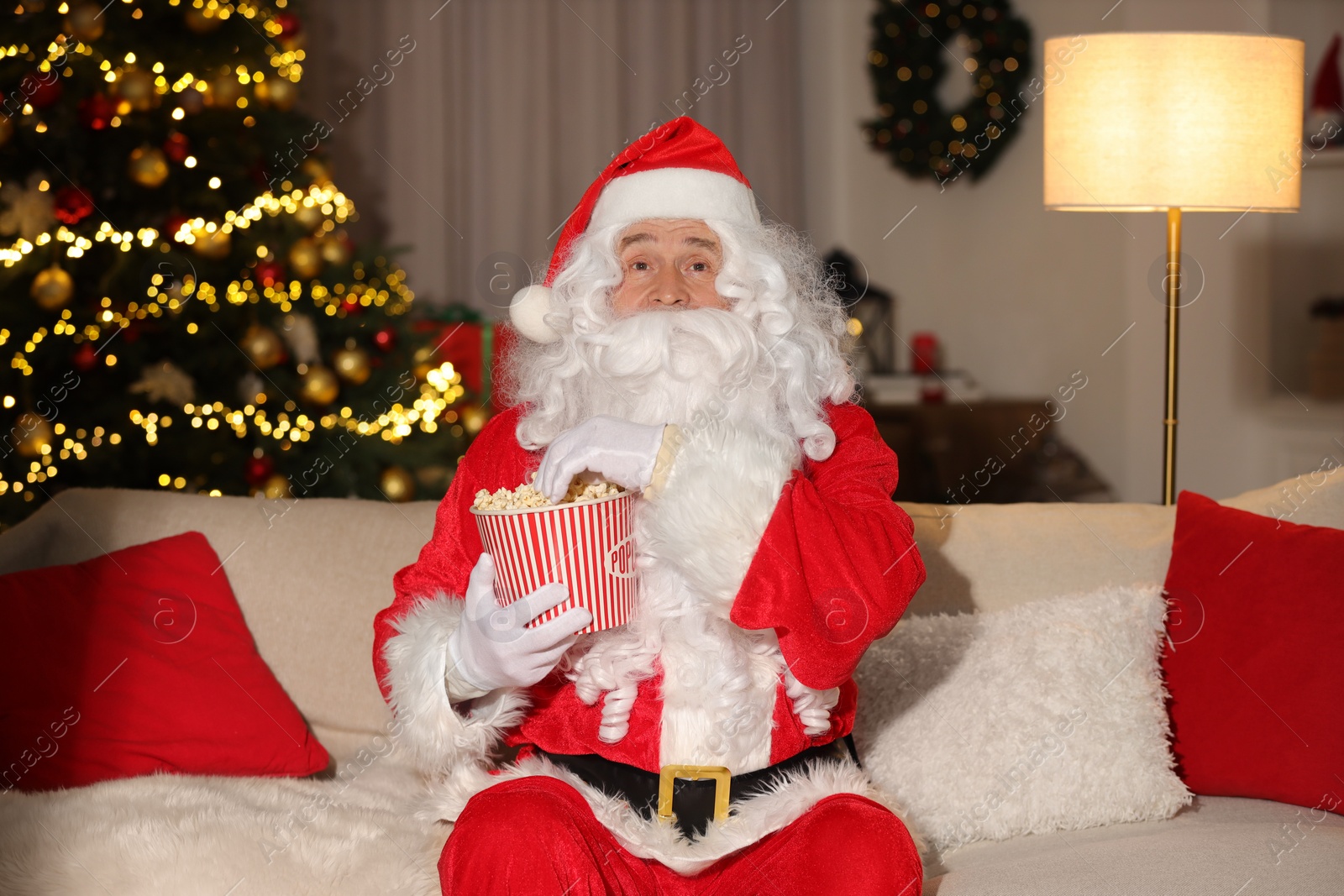 Photo of Merry Christmas. Santa Claus with popcorn bucket watching TV on sofa at home