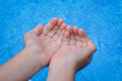 Photo of Girl holding water in hands above pool, closeup