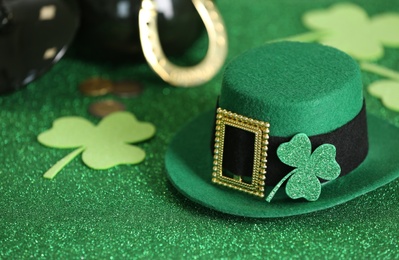 Photo of Leprechaun hat and clover leaves on green glitter background, space for text. St Patrick's Day celebration