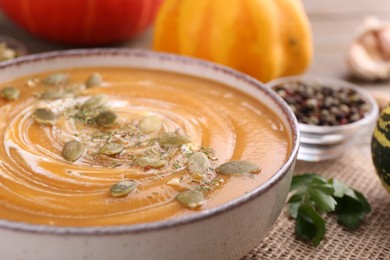 Bowl of delicious pumpkin soup with seeds and cream on table, closeup