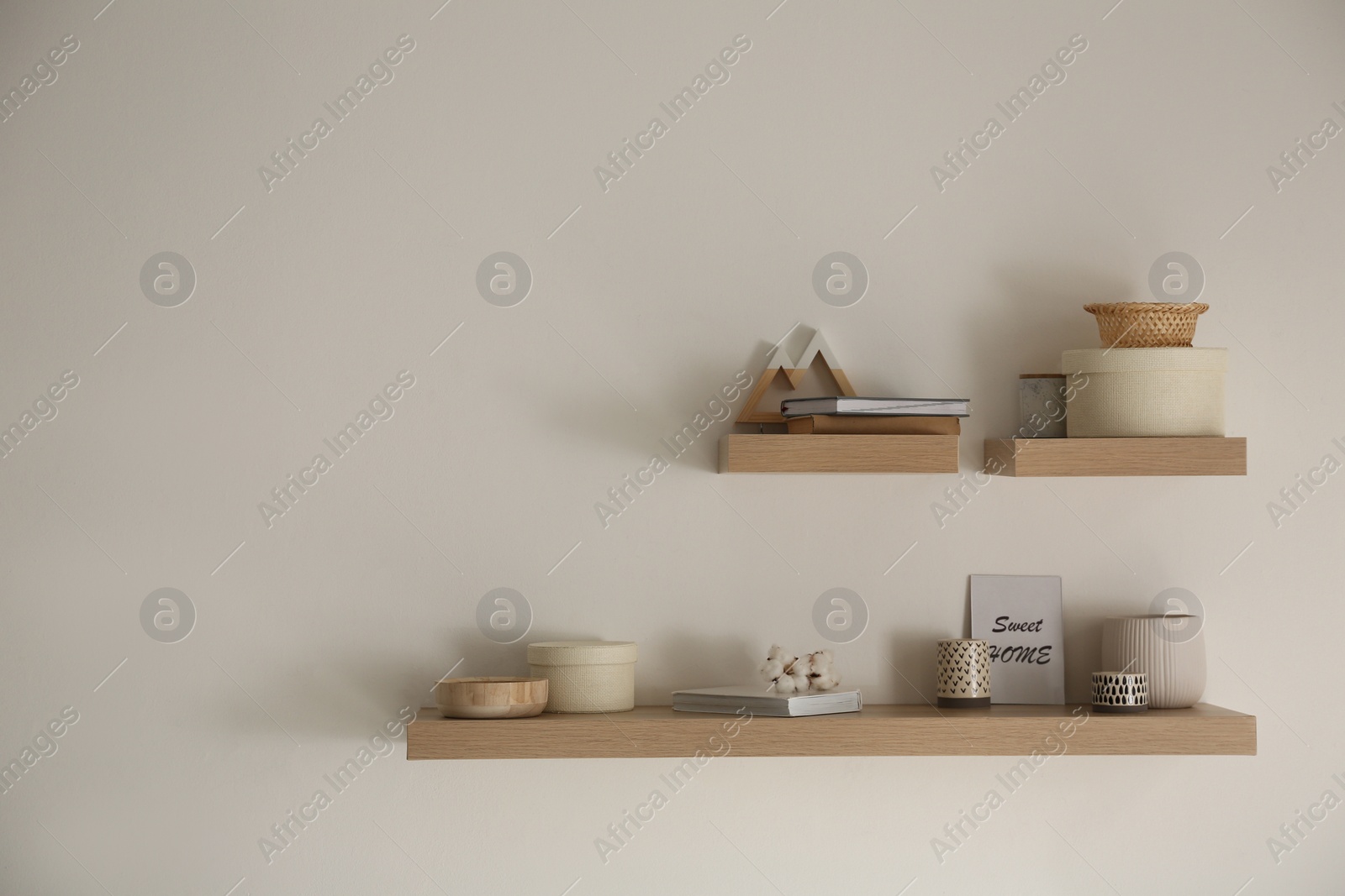 Photo of Wooden shelves with books and different decorative elements on light wall. Space for text