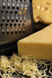 Photo of Grated, cut cheese and grater on black table, closeup