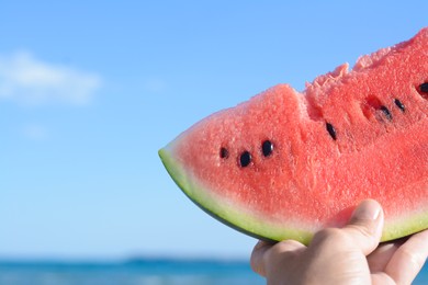 Child holding slice of fresh juicy watermelon near sea outdoors, closeup. Space for text