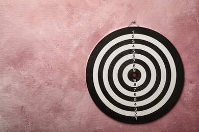 Photo of Dart board hanging on pink textured wall. Space for text