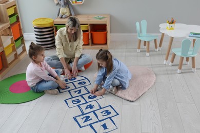 Photo of Mother and little girls taping sticker hopscotch on floor at home