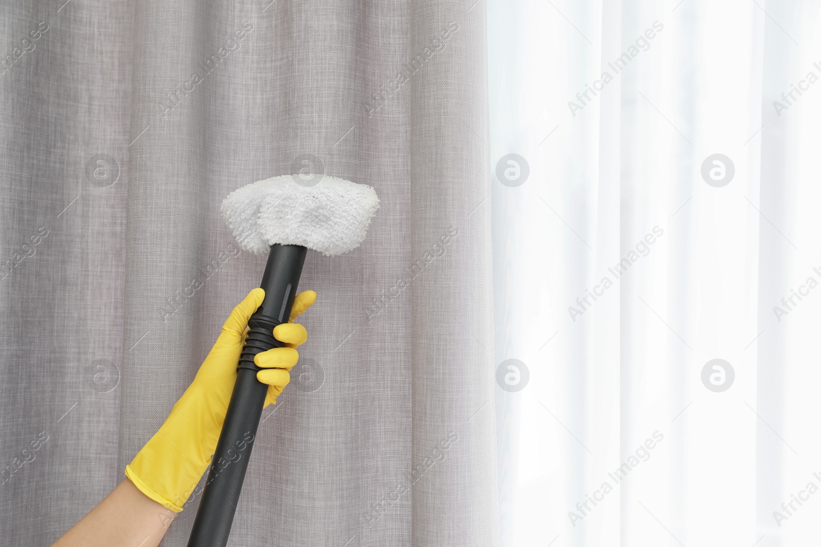 Photo of Janitor removing dust from curtain with steam cleaner indoors, closeup