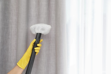 Photo of Janitor removing dust from curtain with steam cleaner indoors, closeup