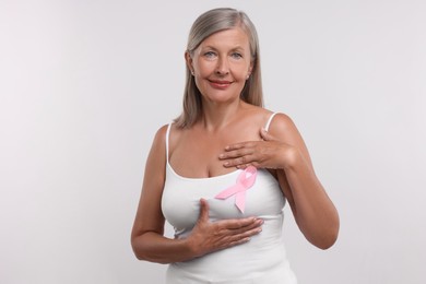 Photo of Beautiful senior woman with pink ribbon on white background. Breast cancer awareness