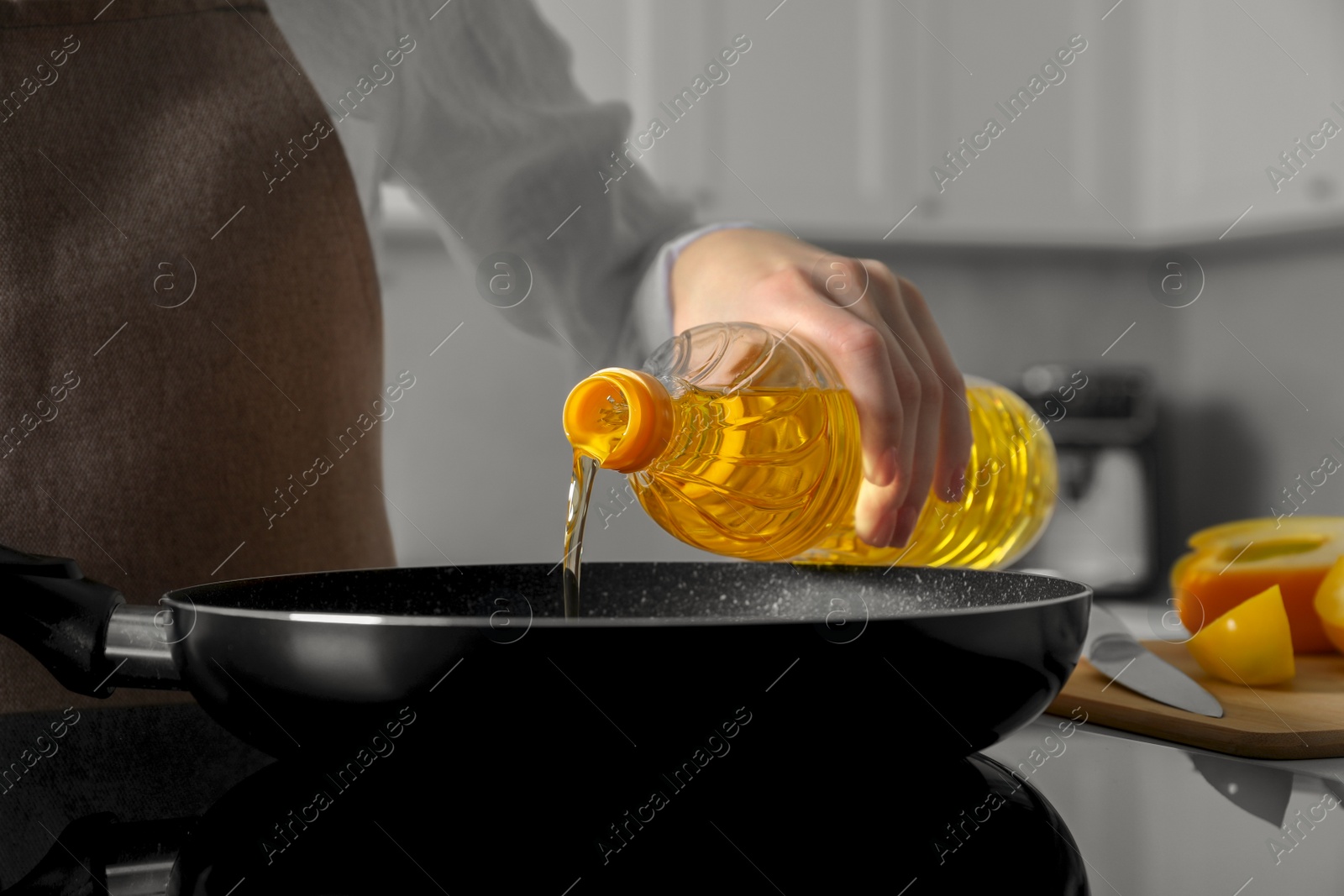 Photo of Woman pouring cooking oil from bottle into frying pan on stove, closeup