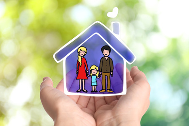 Image of Woman demonstrating illustration of house with family on blurred green background, closeup