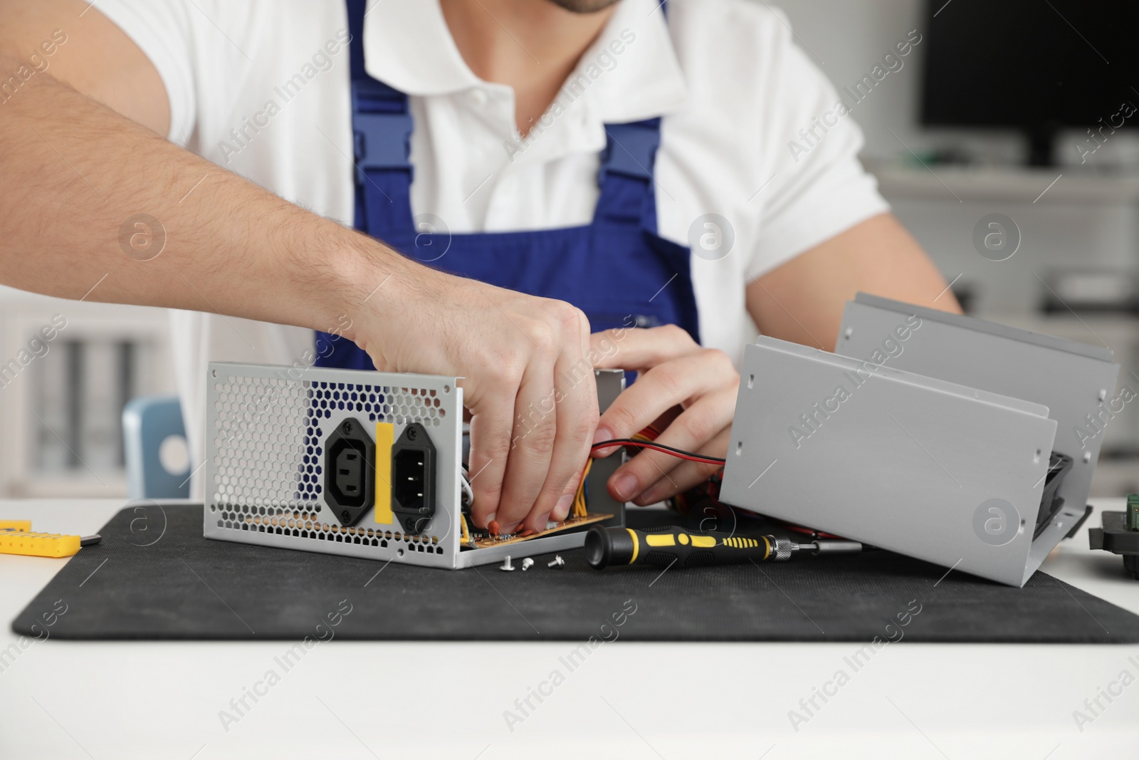 Photo of Male technician repairing power supply unit at table indoors, closeup