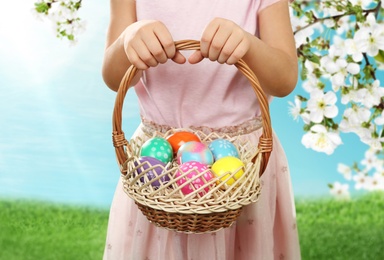Image of Little girl with basket full of Easter eggs on green grass outdoors, closeup