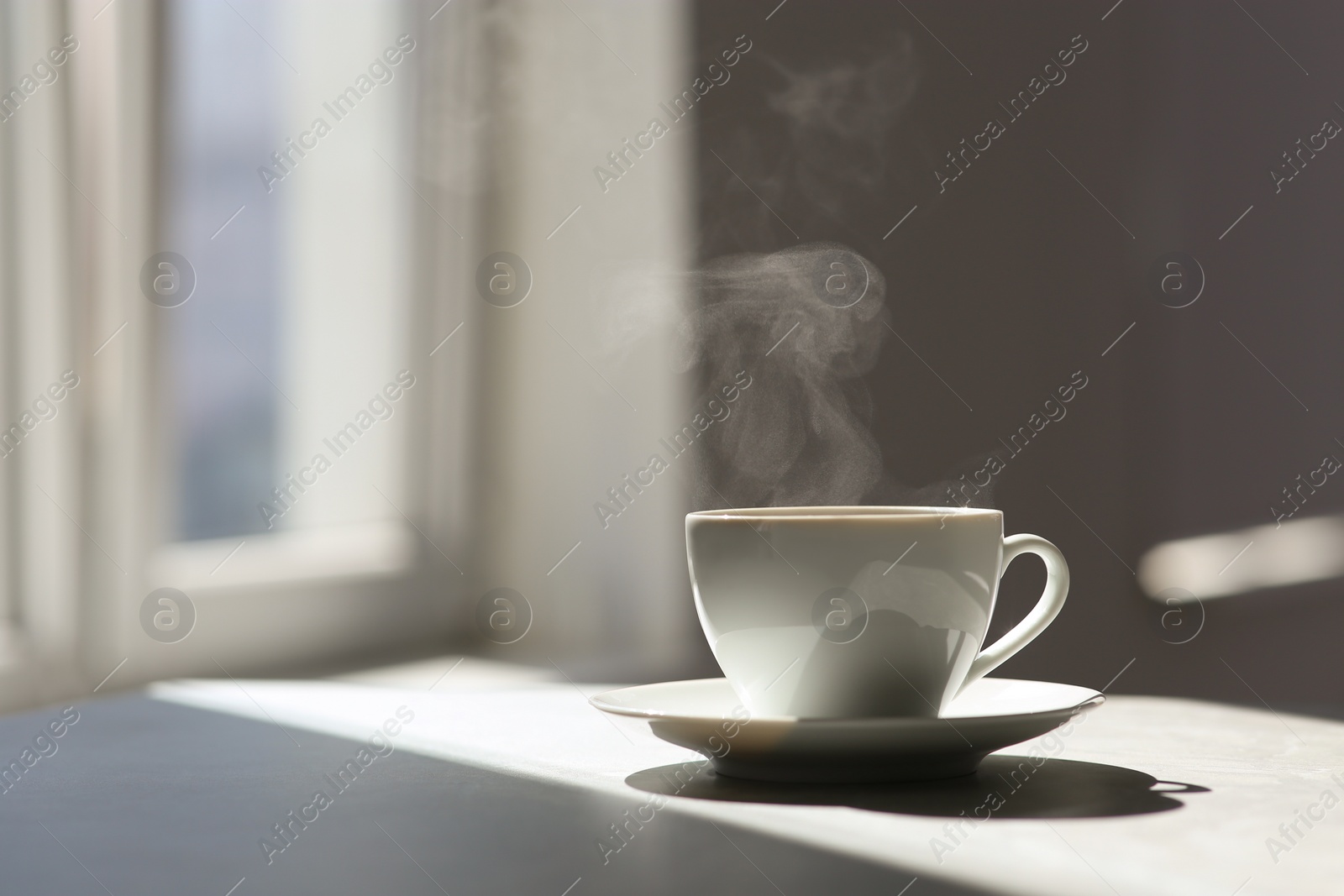 Photo of Cup of delicious coffee on sunlit table, space for text. Good morning