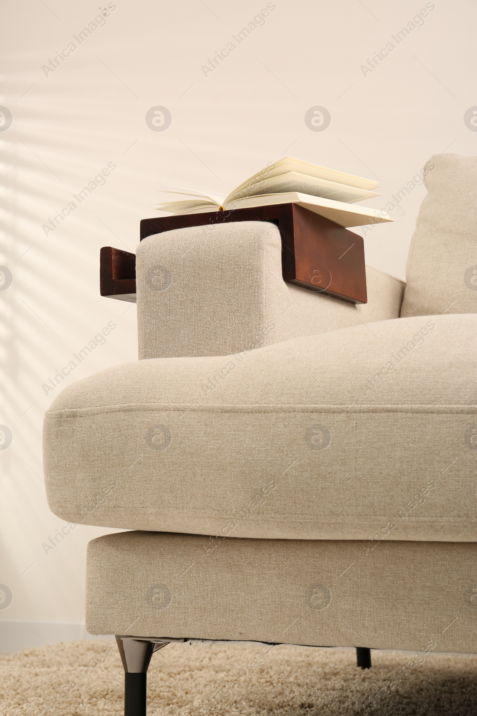 Photo of Open book on sofa with wooden armrest table indoors. Interior element