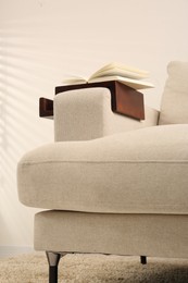 Open book on sofa with wooden armrest table indoors. Interior element