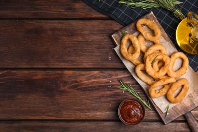 Photo of Fried onion rings served on wooden table, flat lay. Space for text