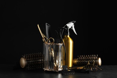 Different hairdresser tools on grey table against black background