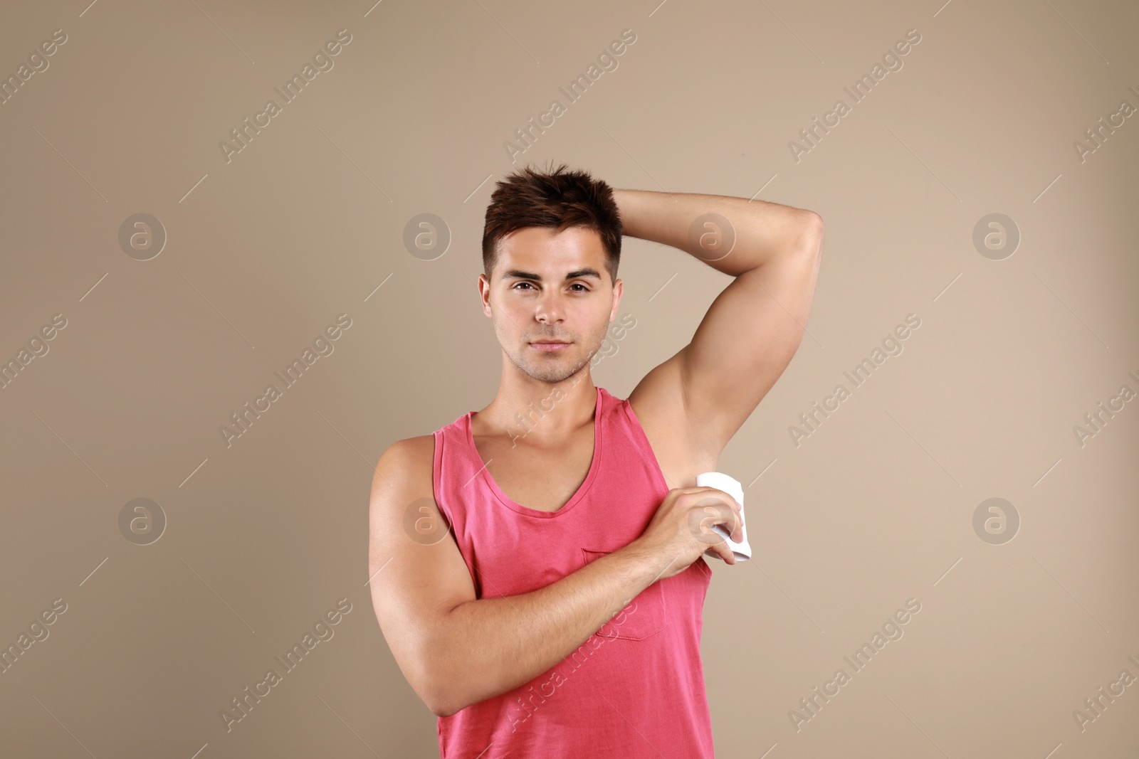 Photo of Young man applying deodorant to armpit on beige background