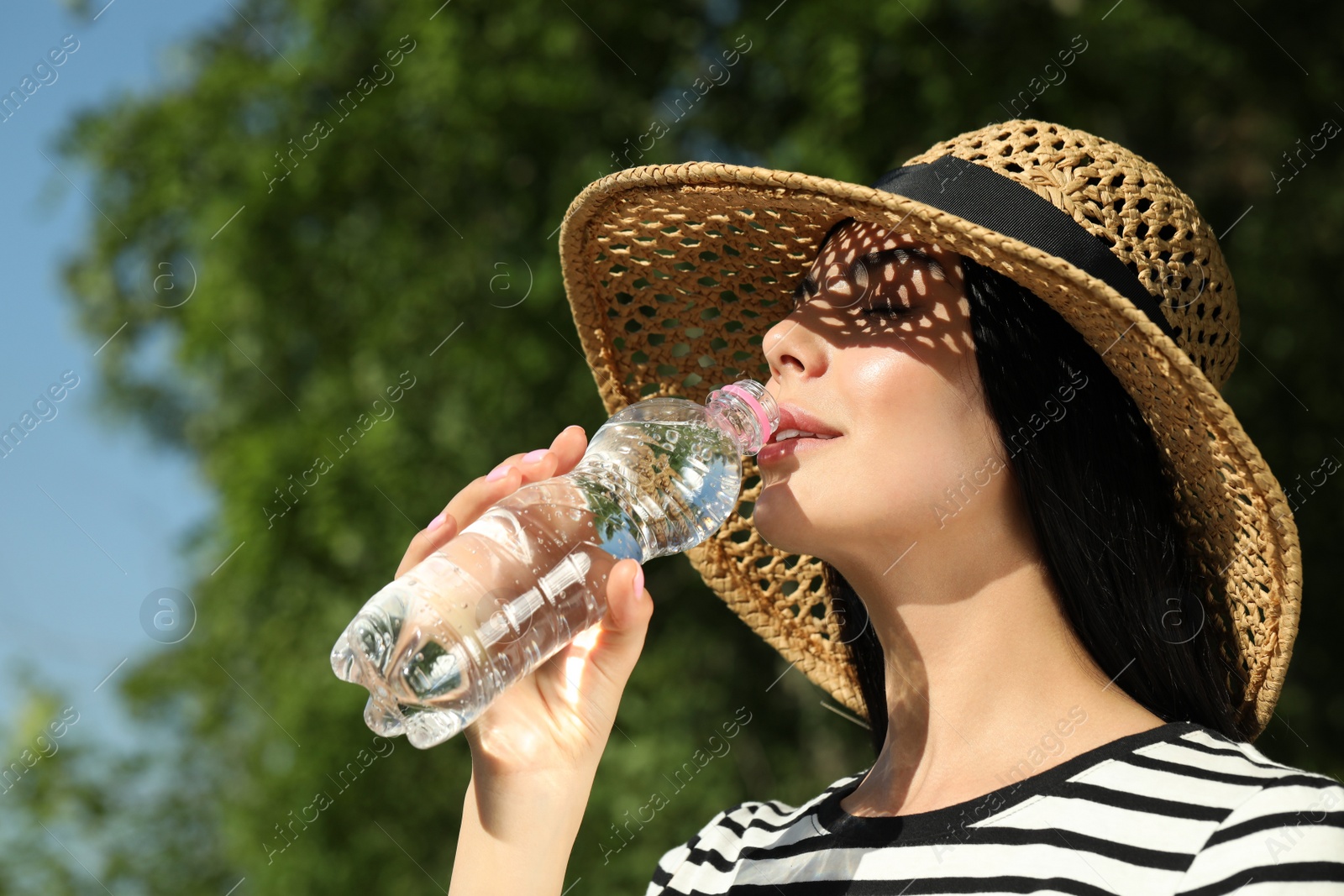 Photo of Beautiful young woman drinking water outdoors. Refreshing drink